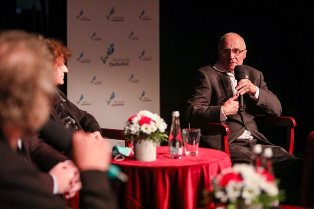 Dwie osoby na oświetlonej teatralnej scenie. Mężczyzna z mikrofonem to Chacky Challot, francuski związkowiec, który w latach 80. pomagał Solidarności. Jego przemówienia słucha Franҫoise Breton – Bałuka.