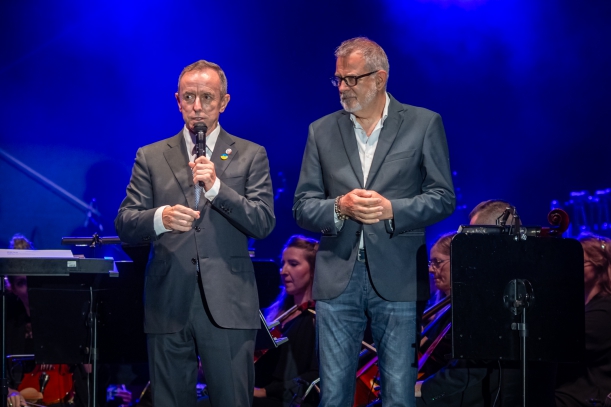 Koncert "Sierpniowe Przełomy" na placu Solidarności w Szczecinie, 27 sierpnia 2023 r. Marszałek Senatu RP Tomasz Grodzki przemawia do mikrofonu. Obok niego na scenie stoi Jacek Jekiel, dyrektor Opery na Zamku w Szczecinie. W tel widać muzyków.