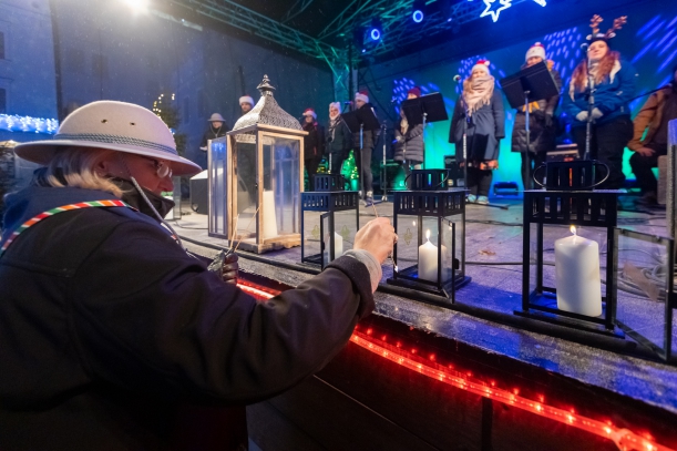 Uroczystość przekazania Betlejemskiego Światła Pokoju mieszkańcom Szczecina i Pomorza Zachodniego. Na dużym dzieńcu Zamku na scenie stoi kilka lampionów. Kobieta w harcerskiej czapce przenosi ogień (drewnianym patyczkiem) na kolejne świece.