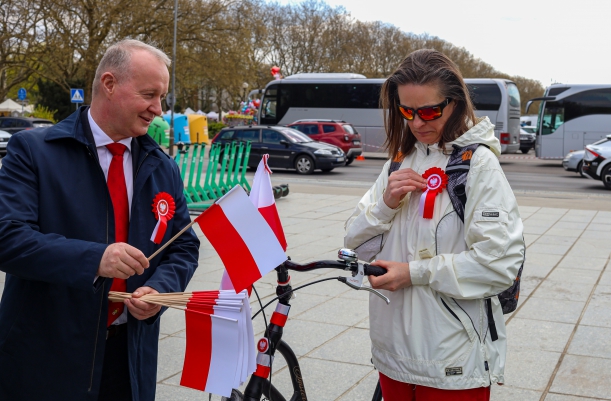 Wicemarszałek Kustosz wręcza flagę i kotylion pani na rowerze.