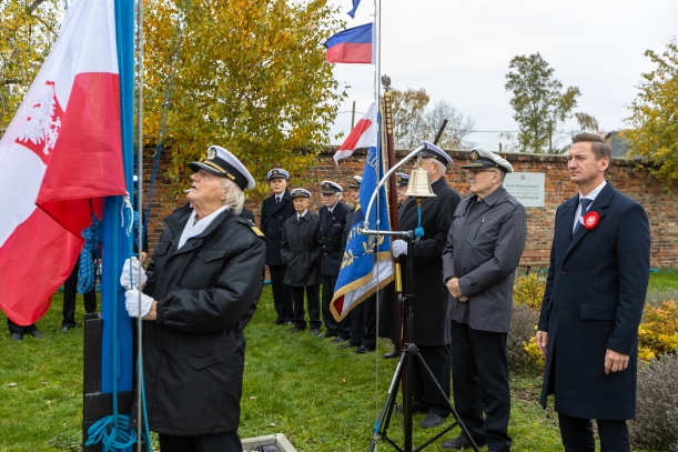 Uroczyste podniesienie polskiej bandery na "kapitańskim maszcie" na Łasztowni w Szczecinie. Przy maszcie - starszy mężczyzna w marynarskiej kurtce. Ceremoniał obserwuje marszałek Olgierg Geblewicz. Obok niego - siedmiu mężczyzn w marynarskich mundurach.