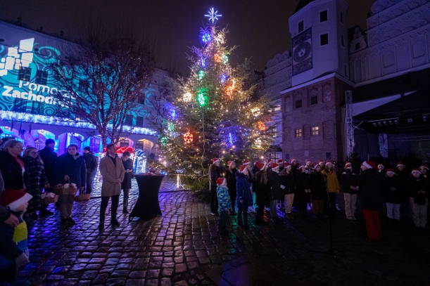 Goście uroczystego odpalenia choinki na Zamku Ksiażąt Pomorskich w Szczecinie, w tle choinka i chó dziecięcy.