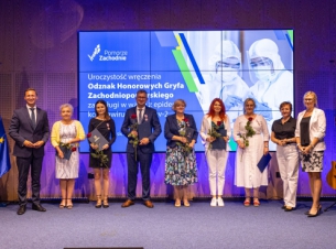 Grupa osób wyróżniona odznakami, nagrodzeni stoją na scenie na tle baneru nawiązująćego do COViD-19