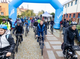 Rowerzyści na starcie rajdu, w tle grupa cyklistów, brama promocyjna Pomorza Zachodniego. 