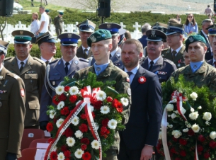 Uroczystości w 78. rocznicę Forsowania Odry na Cmentarzu Wojennym w Starych Łysogórkach. Radny Województwa Artur Nycz stoi na baczność przed pomnikiem, wokół niego żołnierze, policjanci, strażacy w galowych mundurach. Dwóch młodych żołnierze trzyma wieńce