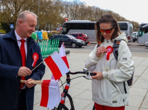 Wicemarszałek Kustosz wręcza flagę i kotylion pani na rowerze. 