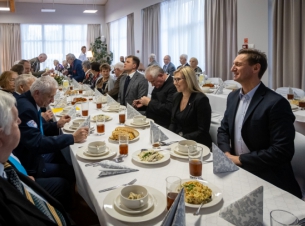 Marszałek Województwa Zachodniopomorskiego Olgierd Geblewicz oraz Członkini Zarządu Województwa Zachodniopomorskiego Anna Bańkowska siedzą za stołem podczas wigilii z kombatantami. Na długim stole biały obrus, świateczne potrawy i stroiki.